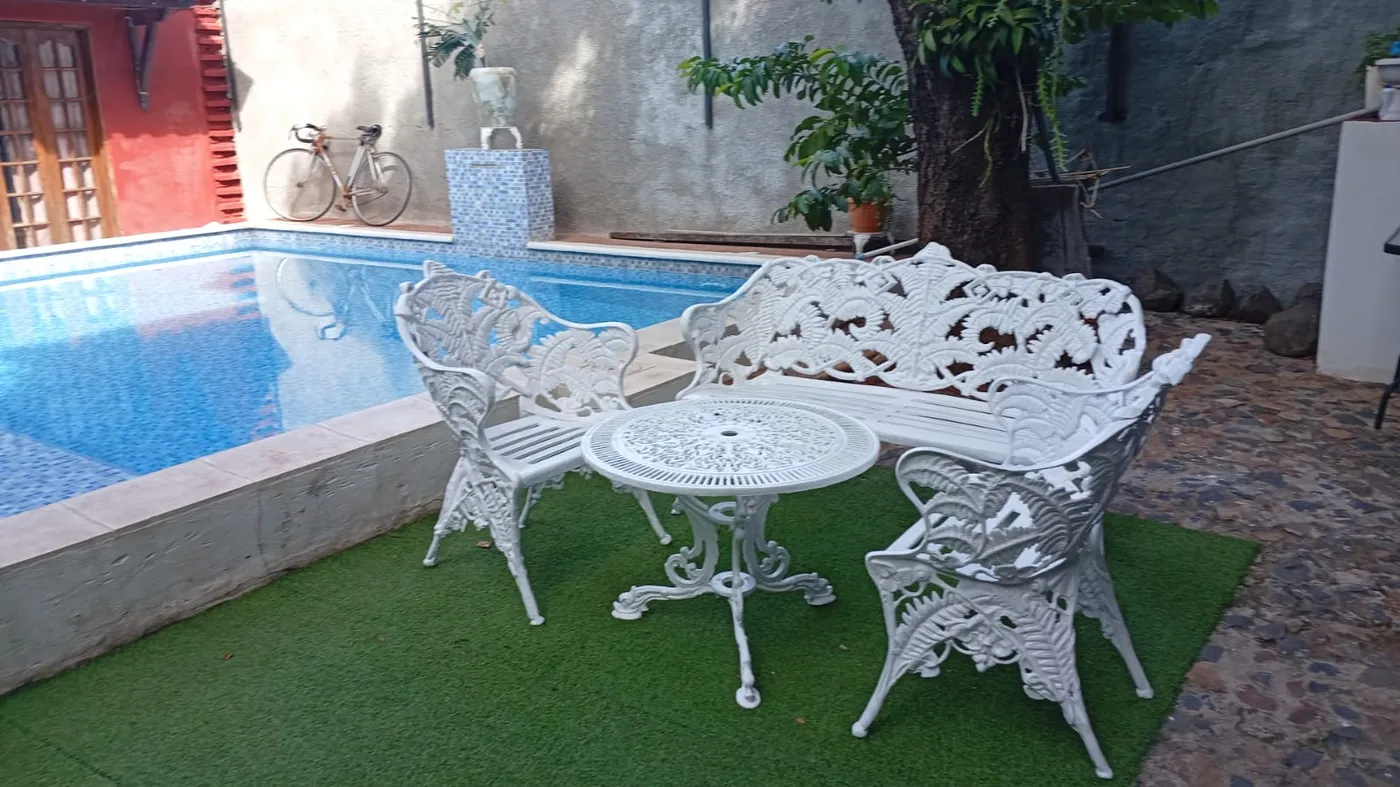 Juego de jardín blanco de fundición calada con mesa y sillones, junto a una pileta con césped sintético