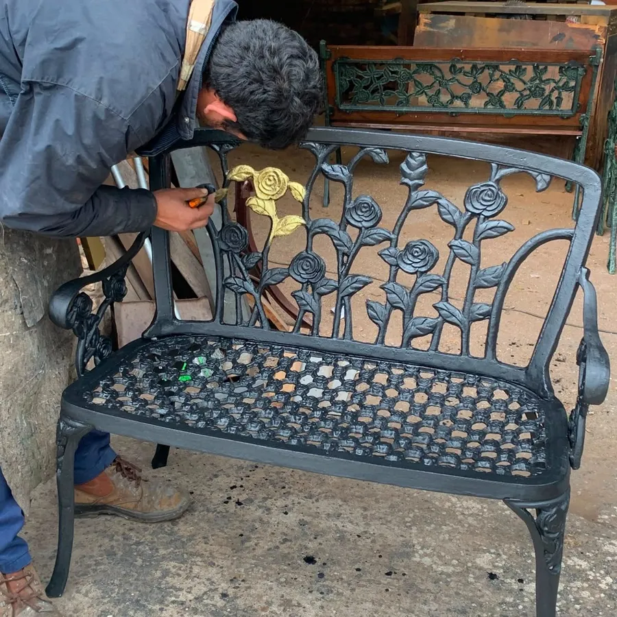 Un operario del taller retoca a pincel una hoja dorada en un banco negro de fundición con rosas caladas